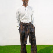 Boot-cut pants featuring a brown and black checkered pattern, a high-waisted design with a large matching fabric waist tie, and a flared leg opening.