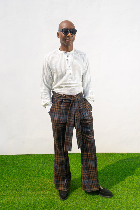 Boot-cut pants featuring a brown and black checkered pattern, a high-waisted design with a large matching fabric waist tie, and a flared leg opening.