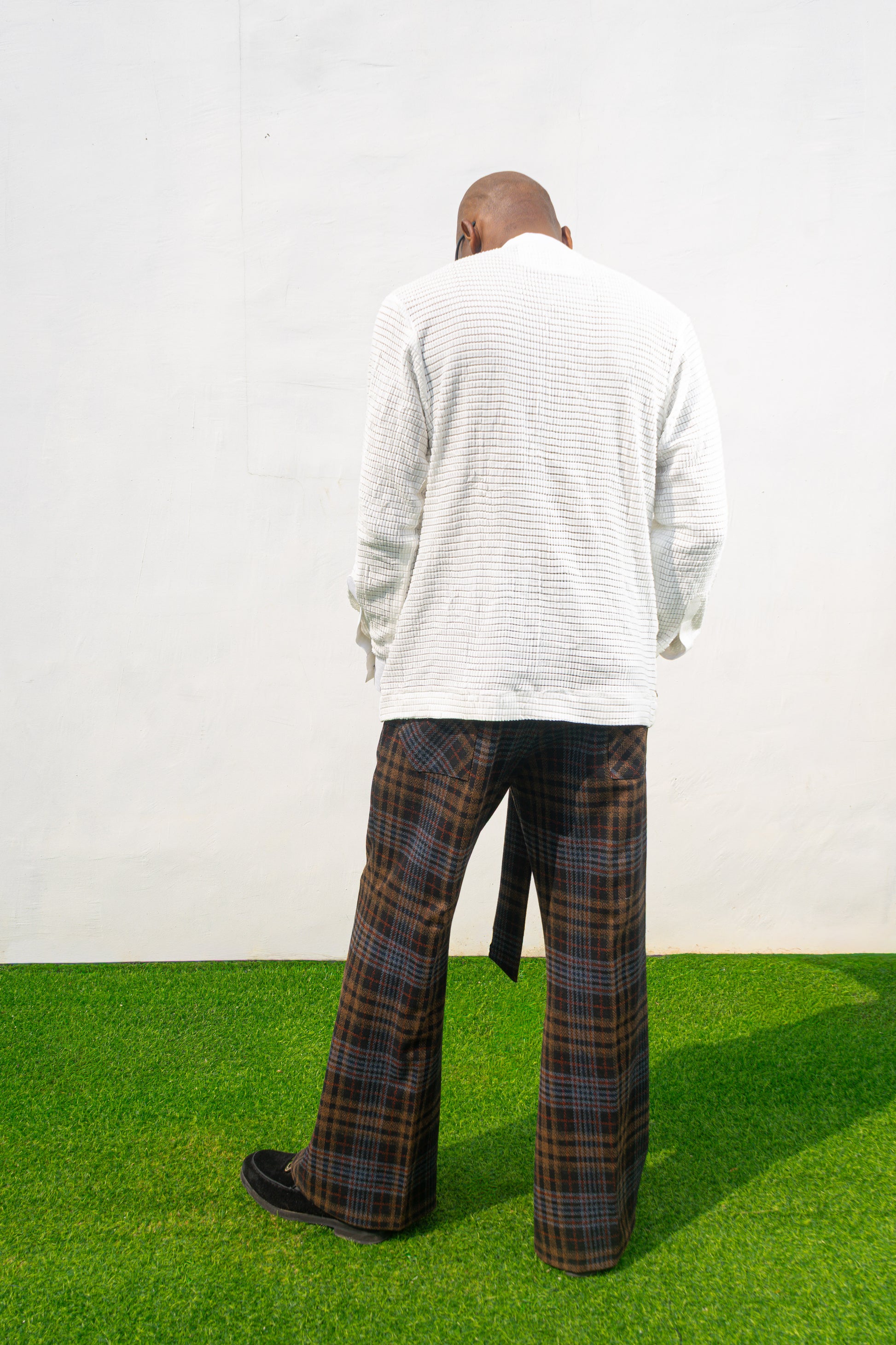 Boot-cut pants featuring a brown and black checkered pattern, a high-waisted design with a large matching fabric waist tie, and a flared leg opening.