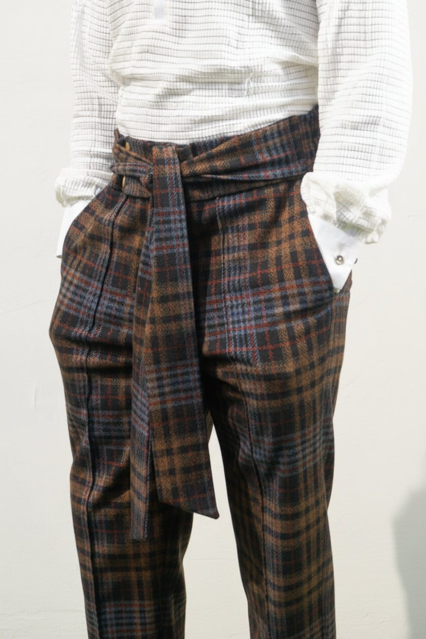 Boot-cut pants featuring a brown and black checkered pattern, a high-waisted design with a large matching fabric waist tie, and a flared leg opening.