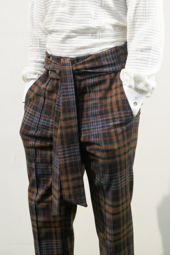 Boot-cut pants featuring a brown and black checkered pattern, a high-waisted design with a large matching fabric waist tie, and a flared leg opening.