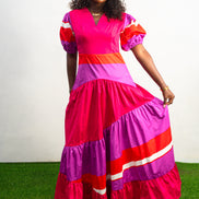 Magenta Sunset Full length Dress featuring a V-neckline, short puff sleeves, and tiered color-block panels in magenta, purple, and orange.