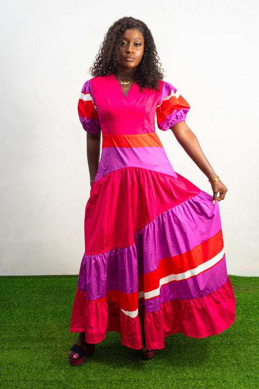 Magenta Sunset Full length Dress featuring a V-neckline, short puff sleeves, and tiered color-block panels in magenta, purple, and orange.