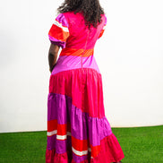 Magenta Sunset Full length Dress featuring a V-neckline, short puff sleeves, and tiered color-block panels in magenta, purple, and orange. Back View