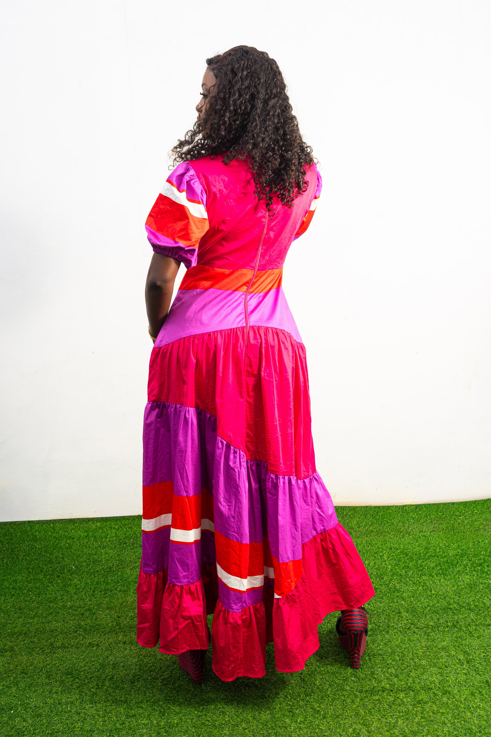 Magenta Sunset Full length Dress featuring a V-neckline, short puff sleeves, and tiered color-block panels in magenta, purple, and orange. Back View