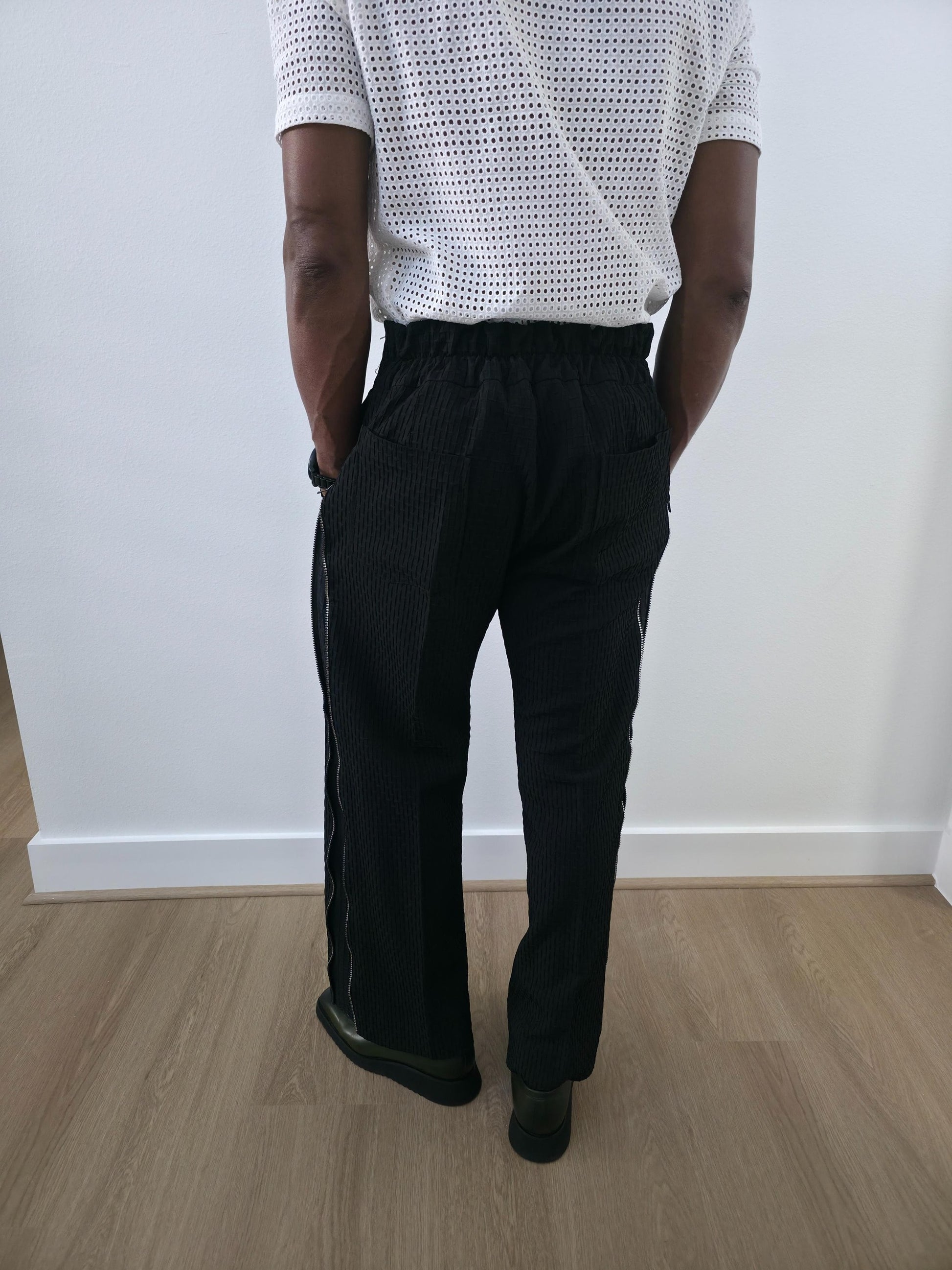 High-Waisted Trousers featuring black micro-textured wide-leg pants with a high structured waistband and side-zip closure. Back View.