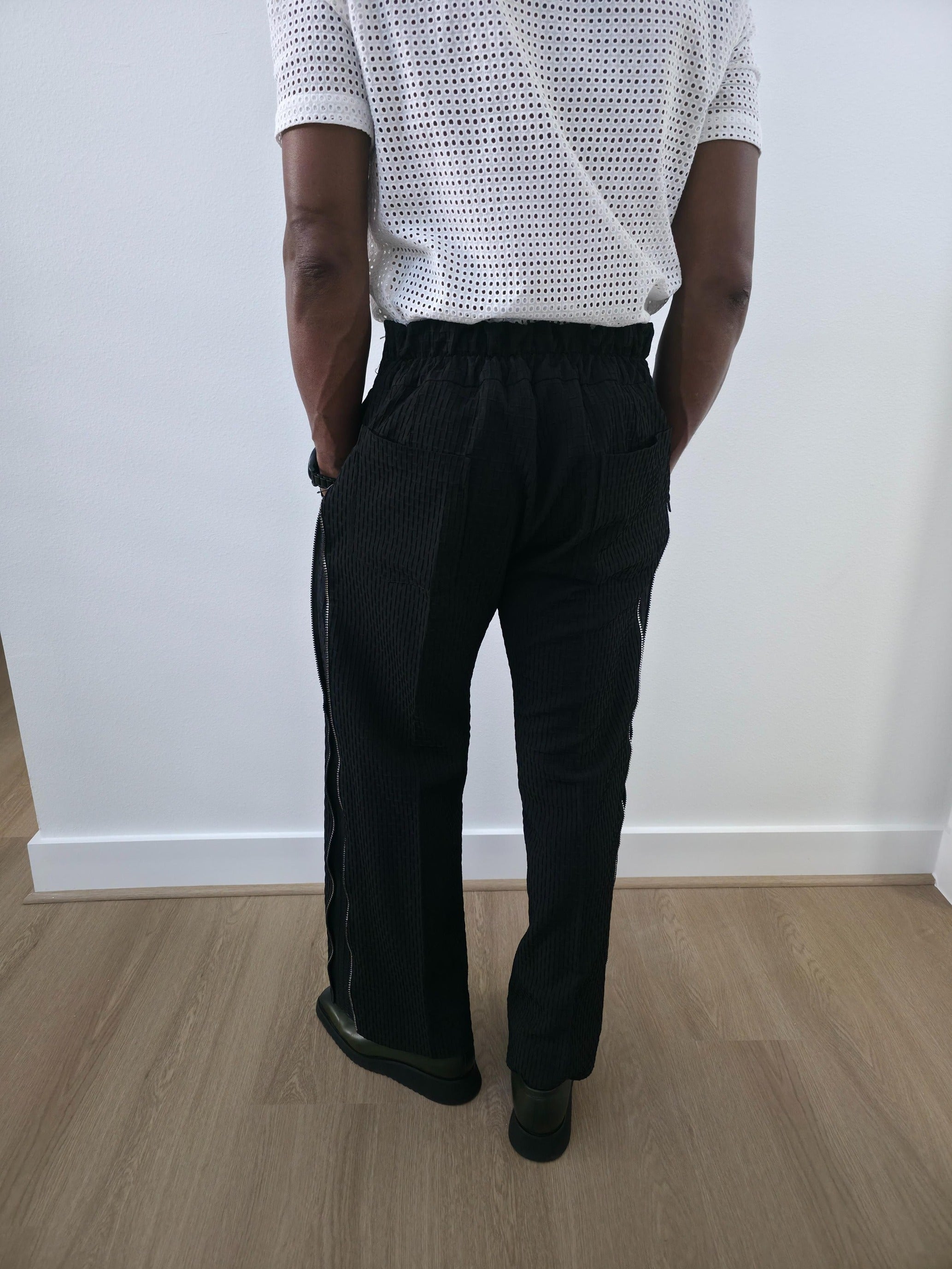High-Waisted Trousers featuring black micro-textured wide-leg pants with a high structured waistband and side-zip closure. Back View.