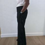 High-Waisted Trousers featuring black micro-textured wide-leg pants with a high structured waistband and side-zip closure. Side View.