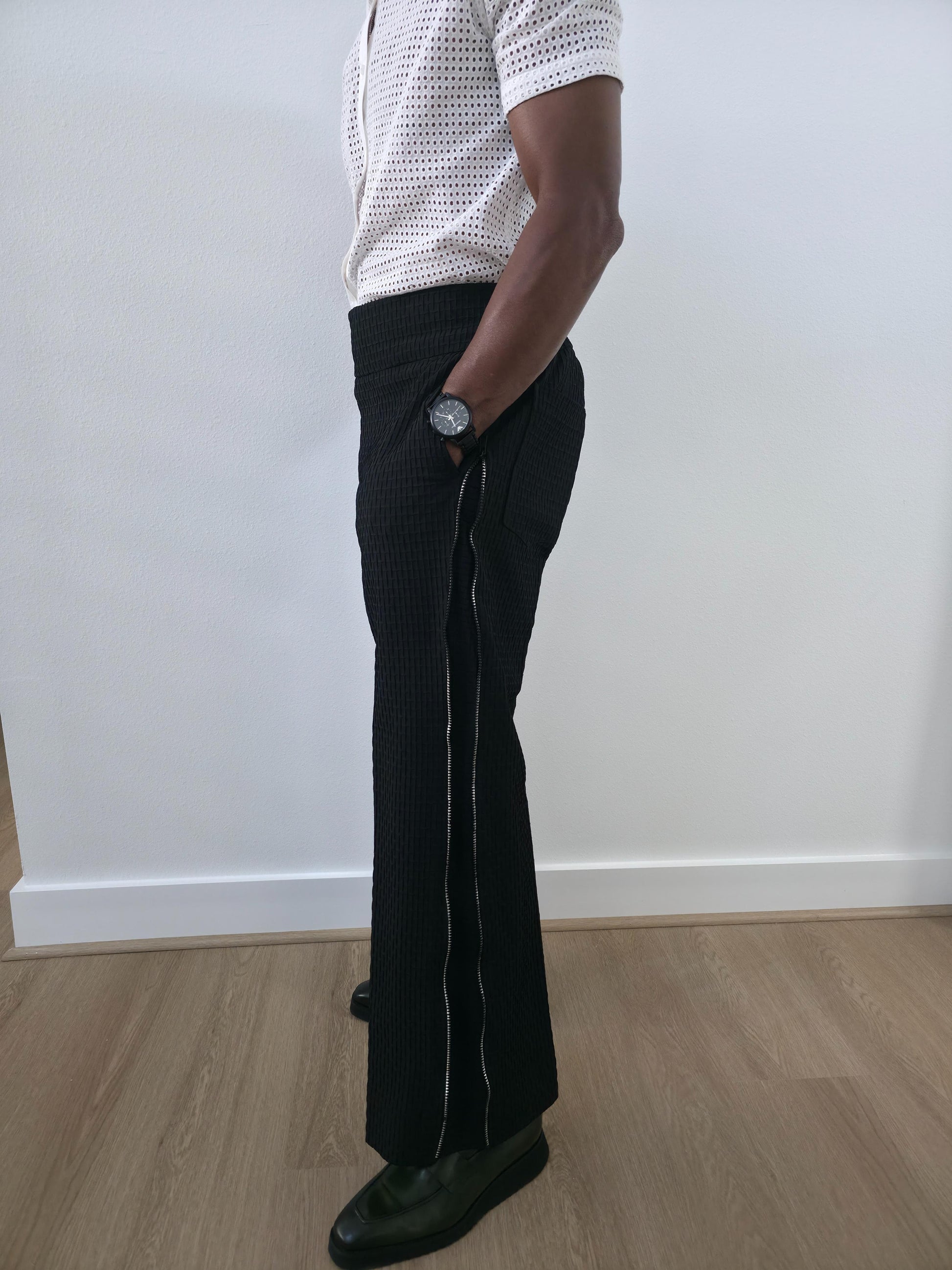 High-Waisted Trousers featuring black micro-textured wide-leg pants with a high structured waistband and side-zip closure. Side View.