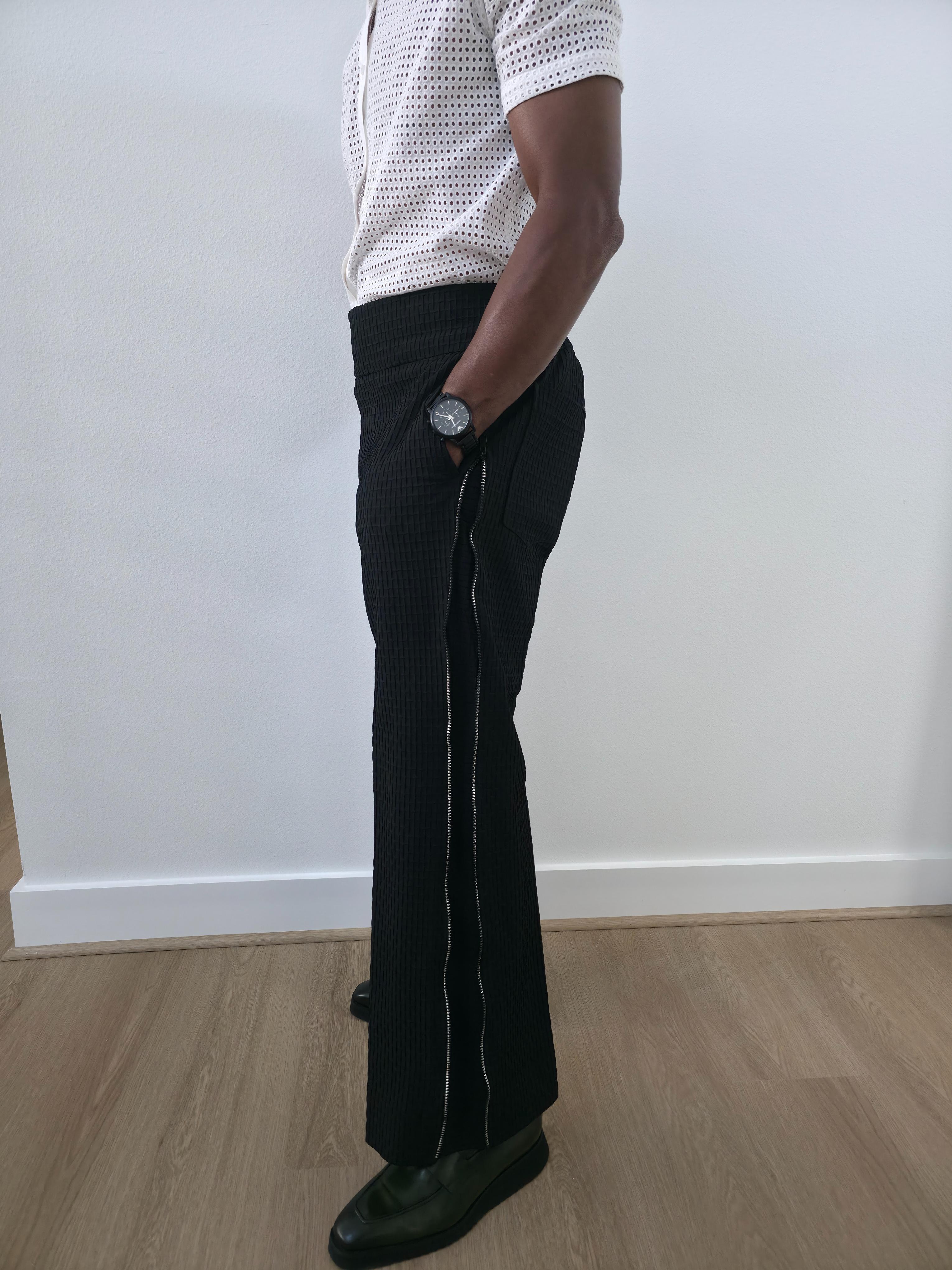 High-Waisted Trousers featuring black micro-textured wide-leg pants with a high structured waistband and side-zip closure. Side View.