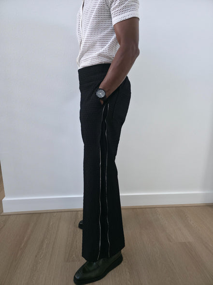 High-Waisted Trousers featuring black micro-textured wide-leg pants with a high structured waistband and side-zip closure. Side View.