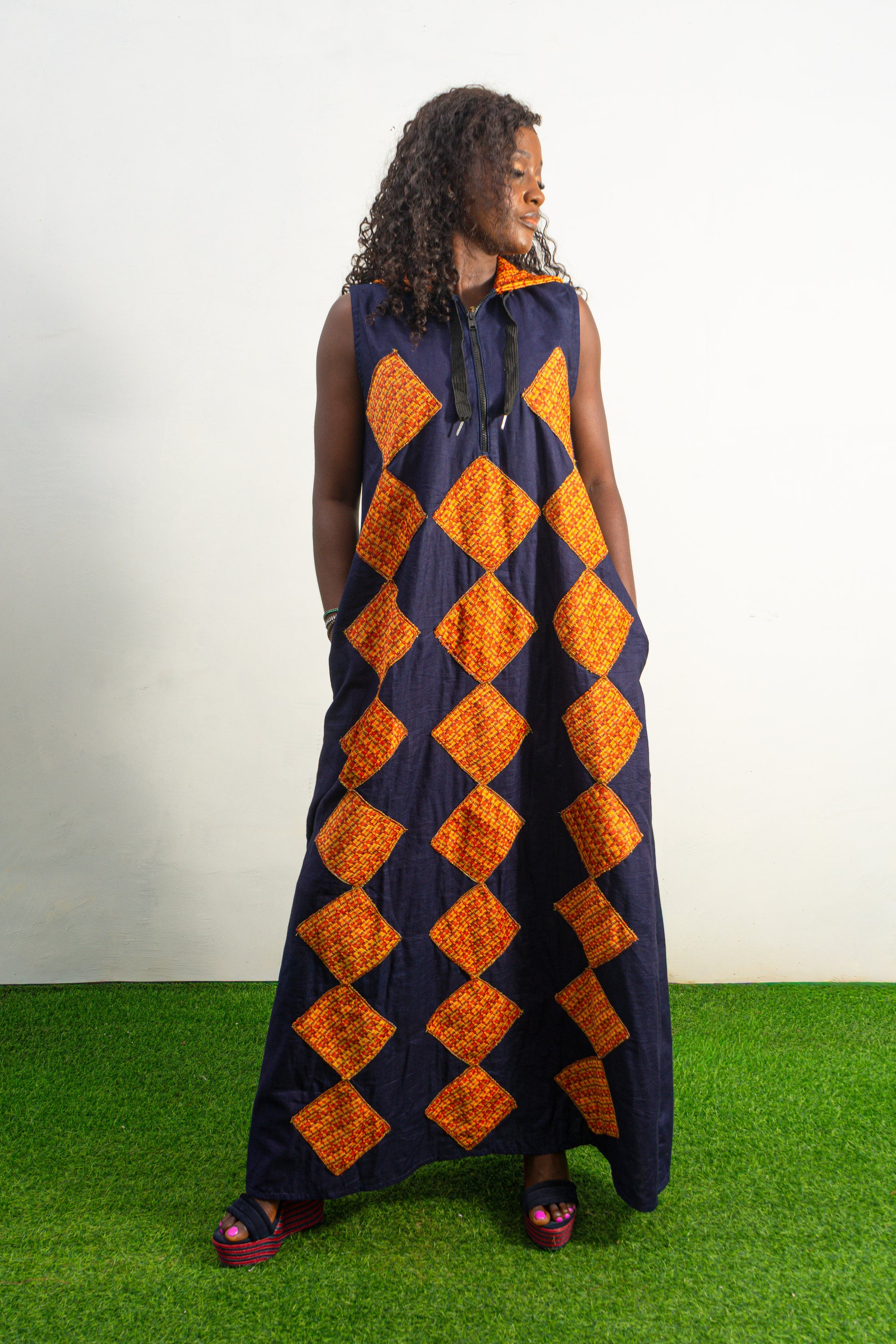 Orange and black Diamond Patterned Jumpsuit featuring a sleeveless black frame with large orange diamond-shaped patchwork across the front and an attached hood. Front View