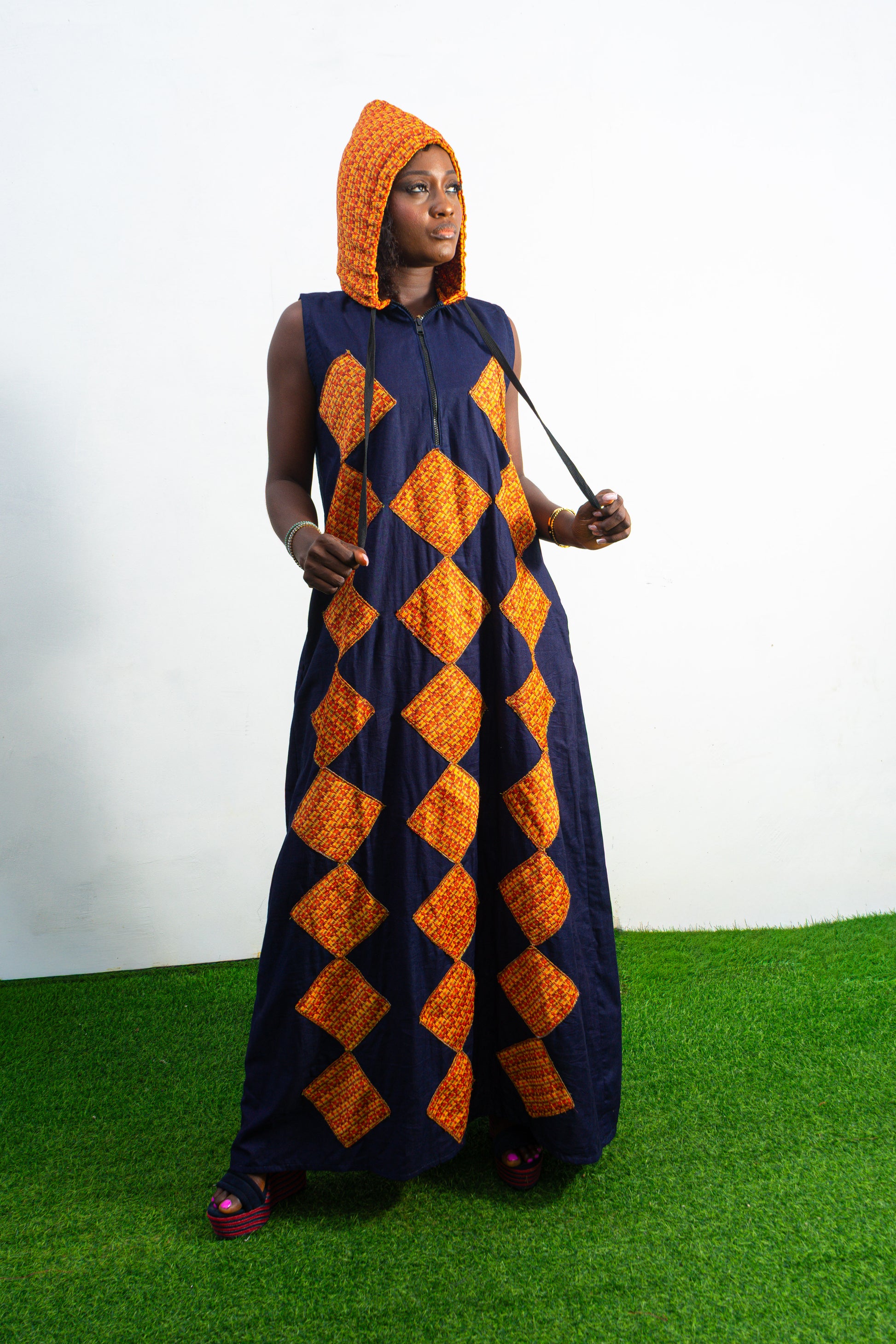 Orange and black Diamond Patterned Jumpsuit featuring a sleeveless black frame with large orange diamond-shaped patchwork across the front and an attached hood. Hoody On