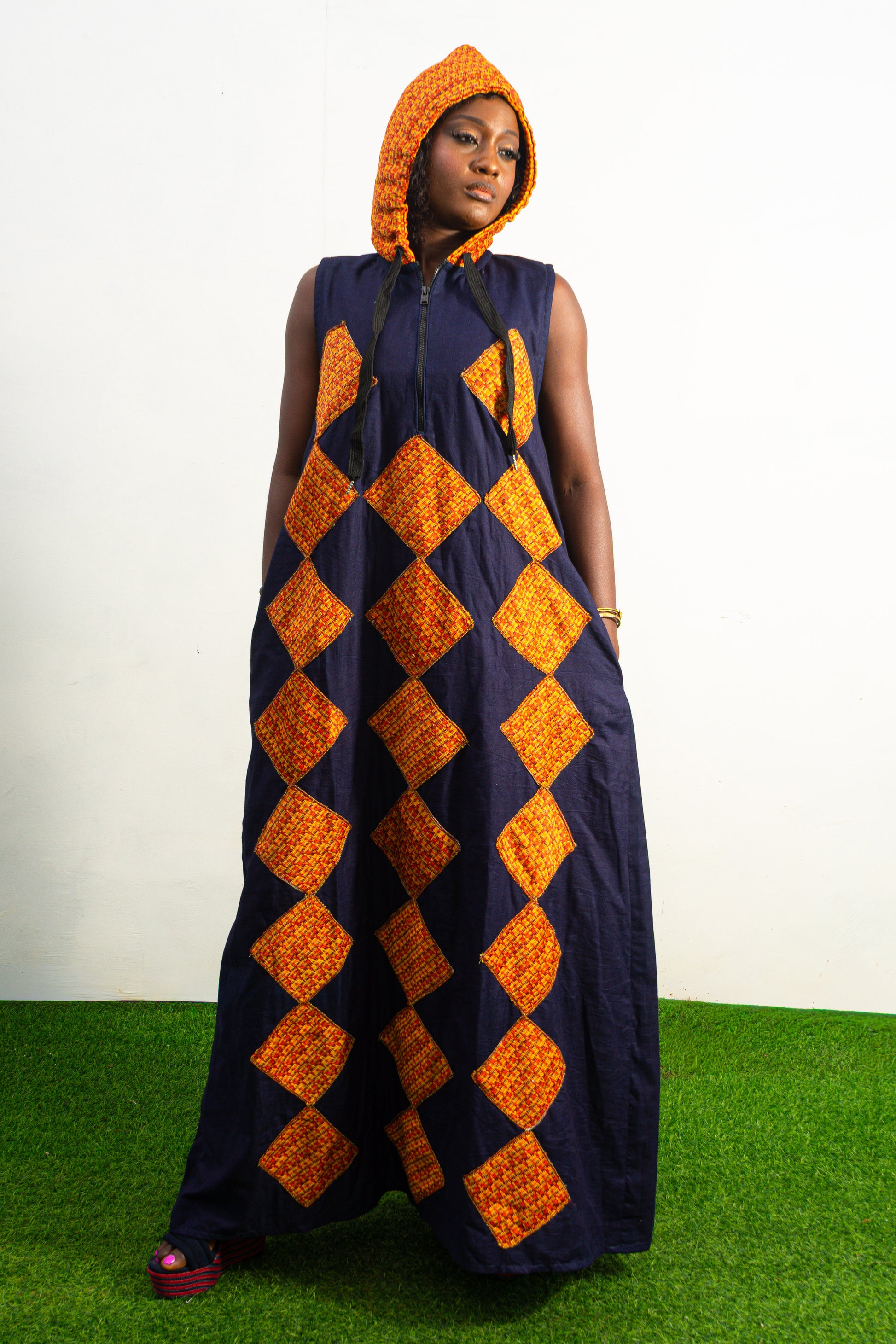 Orange and black Diamond Patterned Jumpsuit featuring a sleeveless black frame with large orange diamond-shaped patchwork across the front and an attached hood. Hoody On Posing