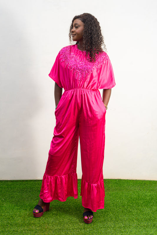 Smocked Pink Jumpsuit  featuring a vibrant fuchsia fabric with a beaded V-shape design on the bodice, short flutter sleeves, and ruffled ankle hems.
