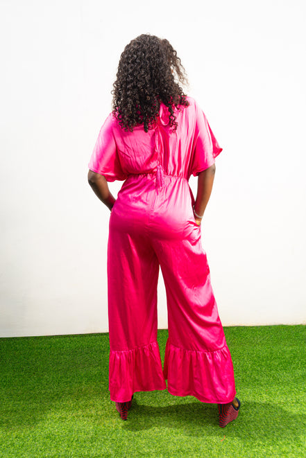 Smocked Pink Jumpsuit featuring a vibrant fuchsia fabric with a beaded V-shape design on the bodice, short flutter sleeves, and ruffled ankle hems. Back View