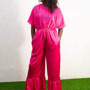 Smocked Pink Jumpsuit featuring a vibrant fuchsia fabric with a beaded V-shape design on the bodice, short flutter sleeves, and ruffled ankle hems. Front View