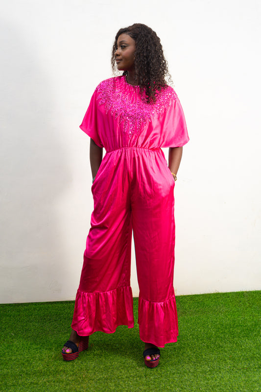Smocked Pink Jumpsuit featuring a vibrant fuchsia fabric with a beaded V-shape design on the bodice, short flutter sleeves, and ruffled ankle hems. Front View