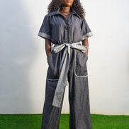 Trendy Denim Jean Jumpsuit featuring a deep indigo denim fabric, light-wash contrast trim on the short sleeves and pockets, and a matching light-wash denim waist tie.
