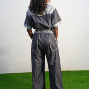 Trendy Denim Jean Jumpsuit featuring a deep indigo denim fabric, light-wash contrast trim on the short sleeves and pockets, and a matching light-wash denim waist tie. Back View