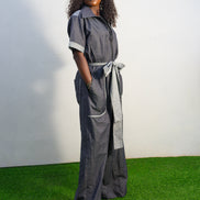 Trendy Denim Jean Jumpsuit (image_8f4b3e.jpg) featuring a deep indigo denim fabric, light-wash contrast trim on the short sleeves and pockets, and a matching light-wash denim waist tie. Side View