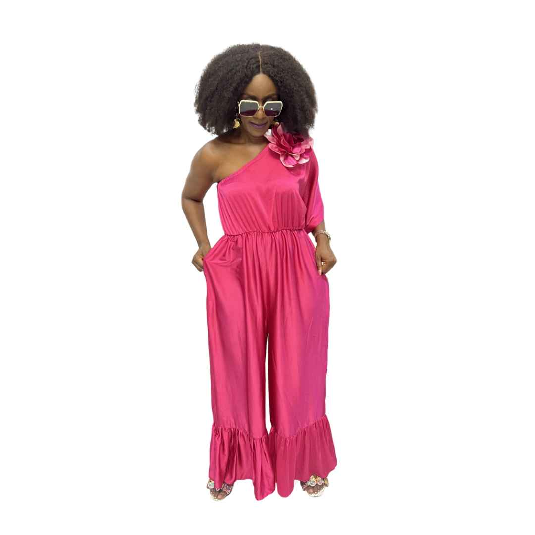 Magenta Jumpsuit featuring a one-shoulder neckline with a large pink floral detail, an elasticated waist, and wide-leg trousers with ruffled hems.
