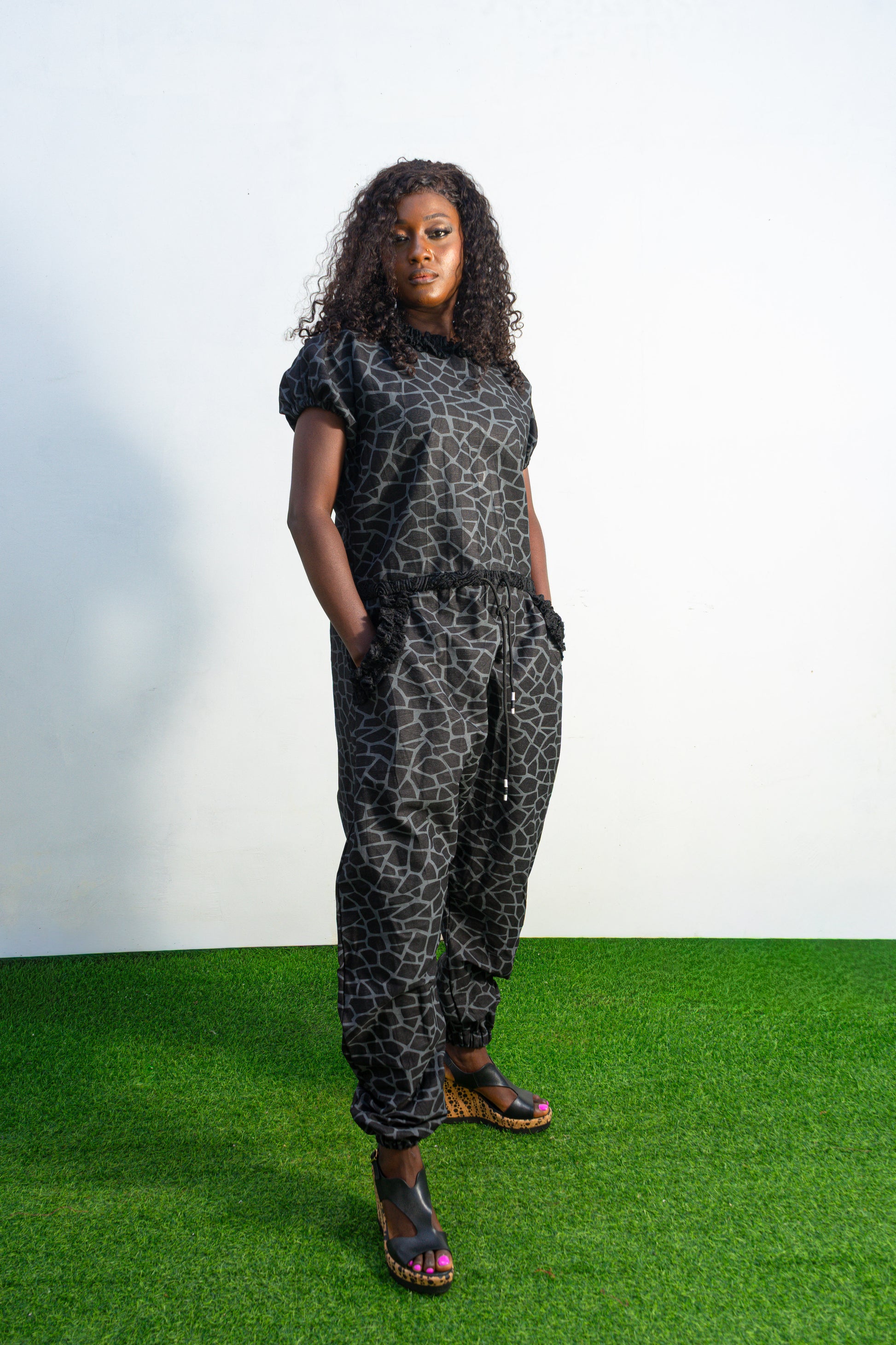 Trendy Animal Print Jumpsuit featuring a dark grey and black geometric giraffe print, short puffed sleeves, textured fringe accents on the collar and pocket entries, and a drawstring waist.