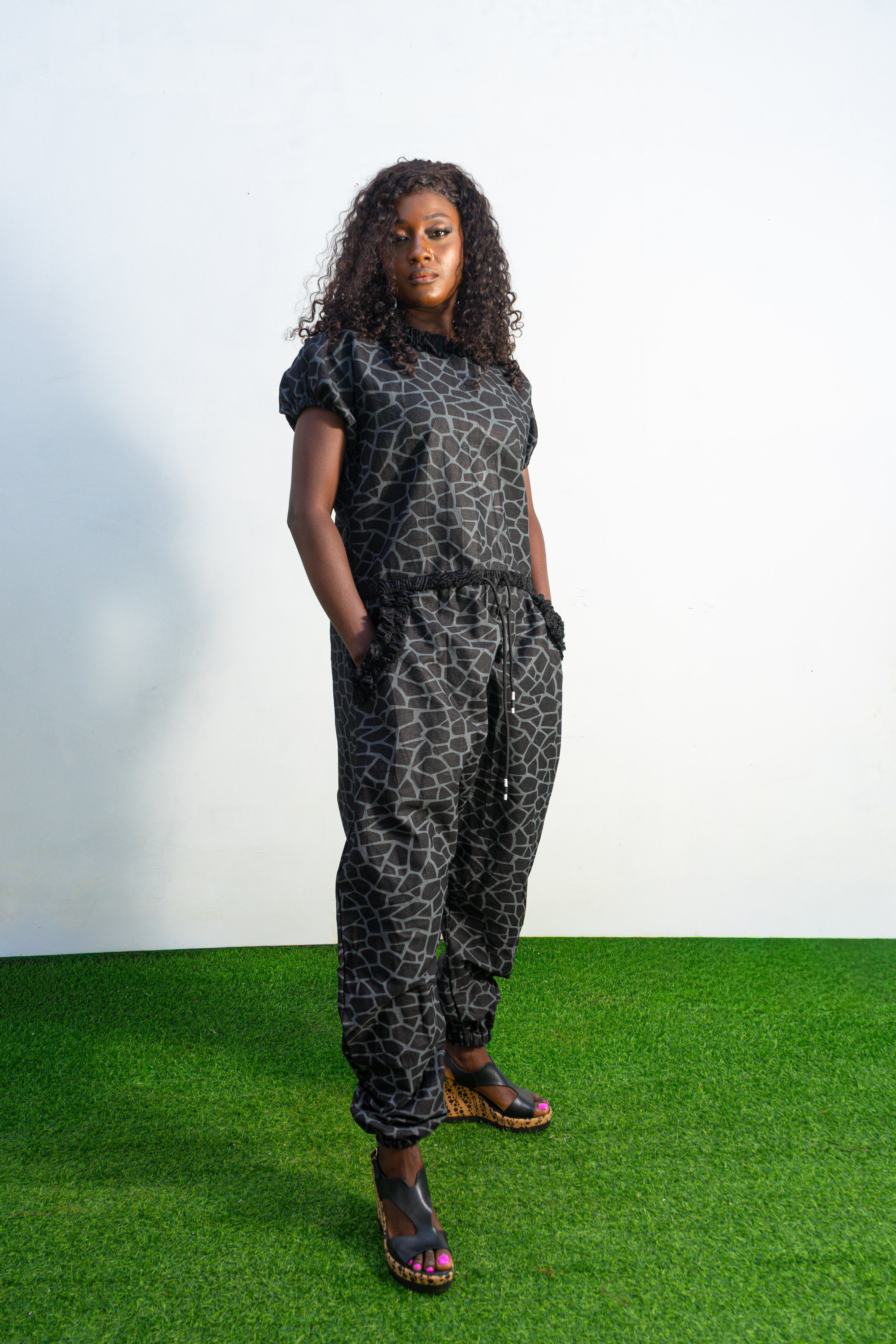 Trendy Animal Print Jumpsuit featuring a dark grey and black geometric giraffe print, short puffed sleeves, textured fringe accents on the collar and pocket entries, and a drawstring waist.