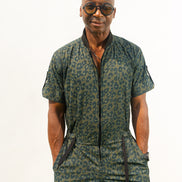 Short-sleeved utility jumpsuit featuring an olive green animal camouflage pattern, a front zipper, and a black bomber-style collar.