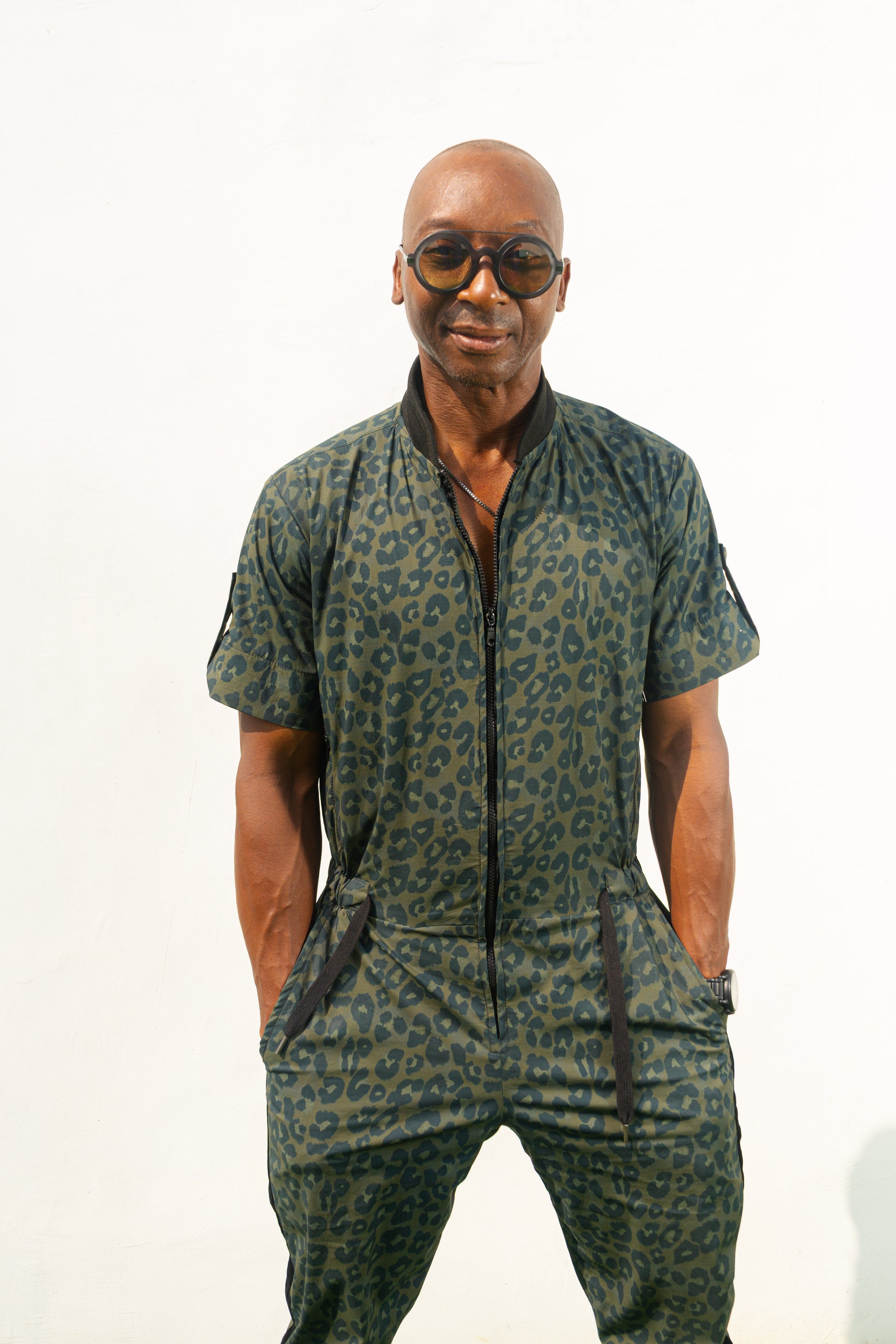 Short-sleeved utility jumpsuit featuring an olive green animal camouflage pattern, a front zipper, and a black bomber-style collar.
