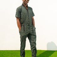 Short-sleeved utility jumpsuit featuring an olive green animal camouflage pattern, a front zipper, and a black bomber-style collar.