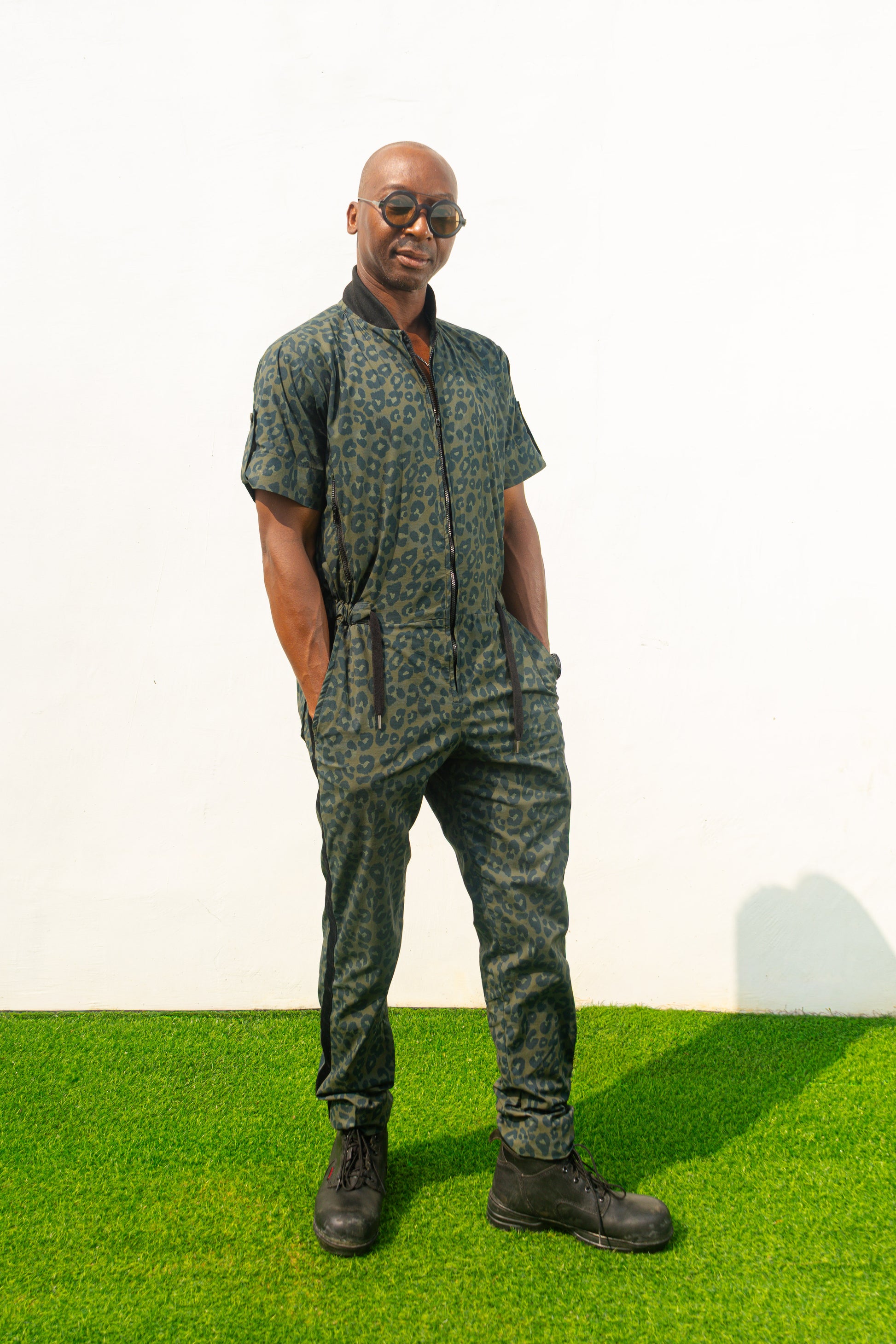 Short-sleeved utility jumpsuit featuring an olive green animal camouflage pattern, a front zipper, and a black bomber-style collar.