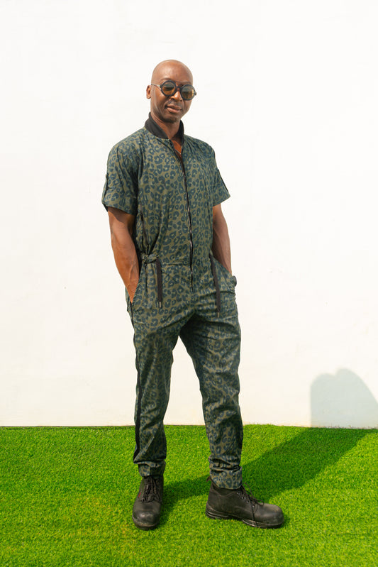 Short-sleeved utility jumpsuit featuring an olive green animal camouflage pattern, a front zipper, and a black bomber-style collar.