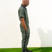 Short-sleeved utility jumpsuit featuring an olive green animal camouflage pattern, a front zipper, and a black bomber-style collar.