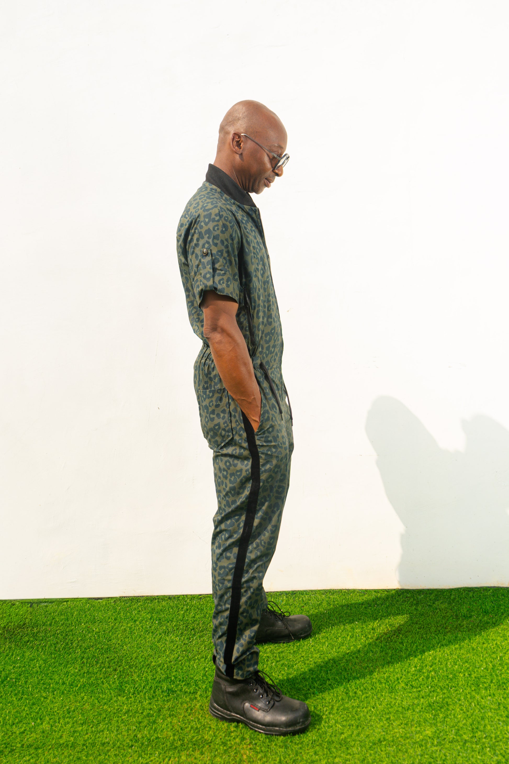 Short-sleeved utility jumpsuit featuring an olive green animal camouflage pattern, a front zipper, and a black bomber-style collar.