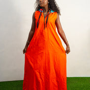 Jumpsuit featuring a vibrant solid orange hue, a deep V-neckline with a metal zipper and black pull cords, and a modern hoodie lined with an intricate, multi-colored Afrocentric pattern.