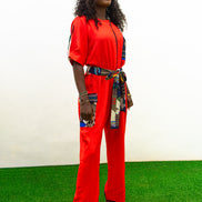 Chic Orange Jumpsuit with a colorful tassel  featuring a bright orange fabric, short sleeves, a patterned chest pocket, and a matching colorful patterned waist belt.