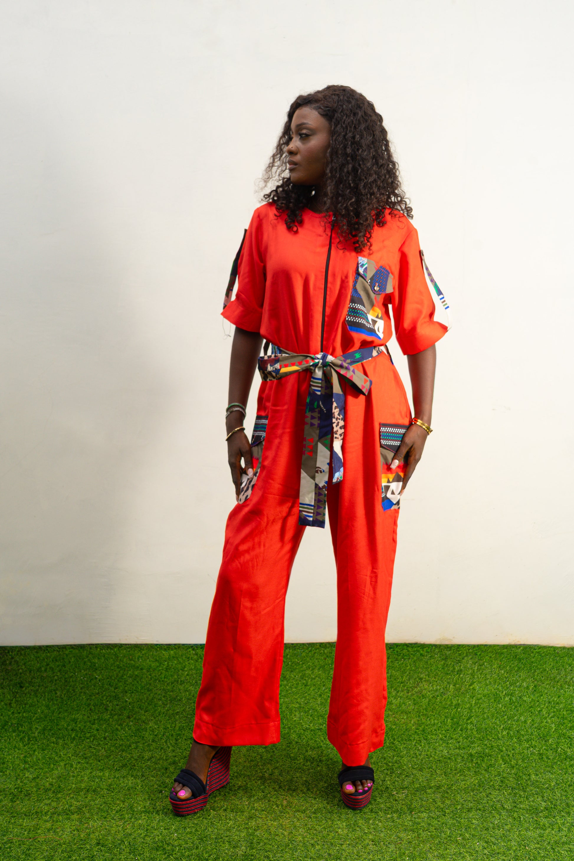 Chic Orange Jumpsuit with a colorful tassel  featuring a bright orange fabric, short sleeves, a patterned chest pocket, and a matching colorful patterned waist belt.  Female's Clothing