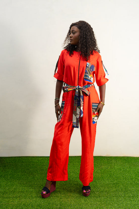 Chic Orange Jumpsuit with a colorful tassel  featuring a bright orange fabric, short sleeves, a patterned chest pocket, and a matching colorful patterned waist belt.  Female's Clothing