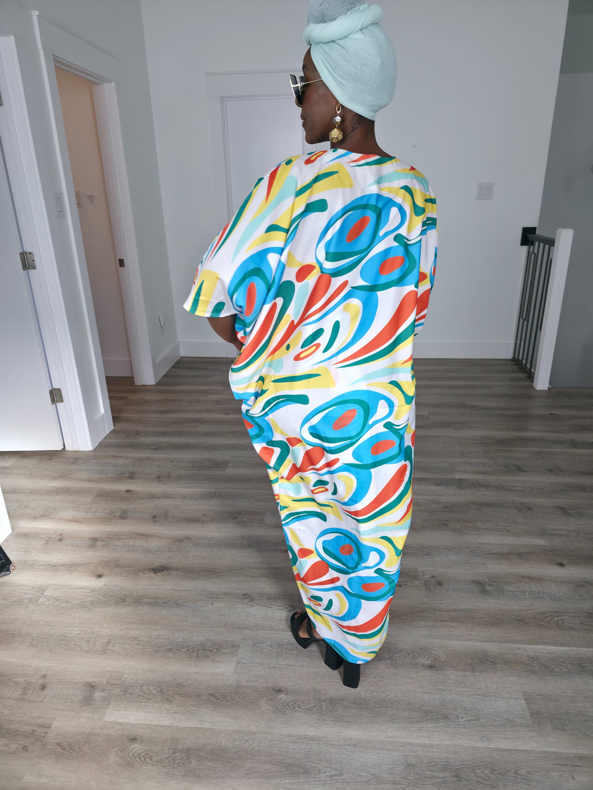 Abstract Aurora Boubou Kaftan featuring a colorful turquoise, orange, and yellow swirl pattern on white silk-satin with a mint headwrap. Back View