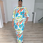 Abstract Aurora Boubou Kaftan featuring a colorful turquoise, orange, and yellow swirl pattern on white silk-satin with a mint headwrap. Front View