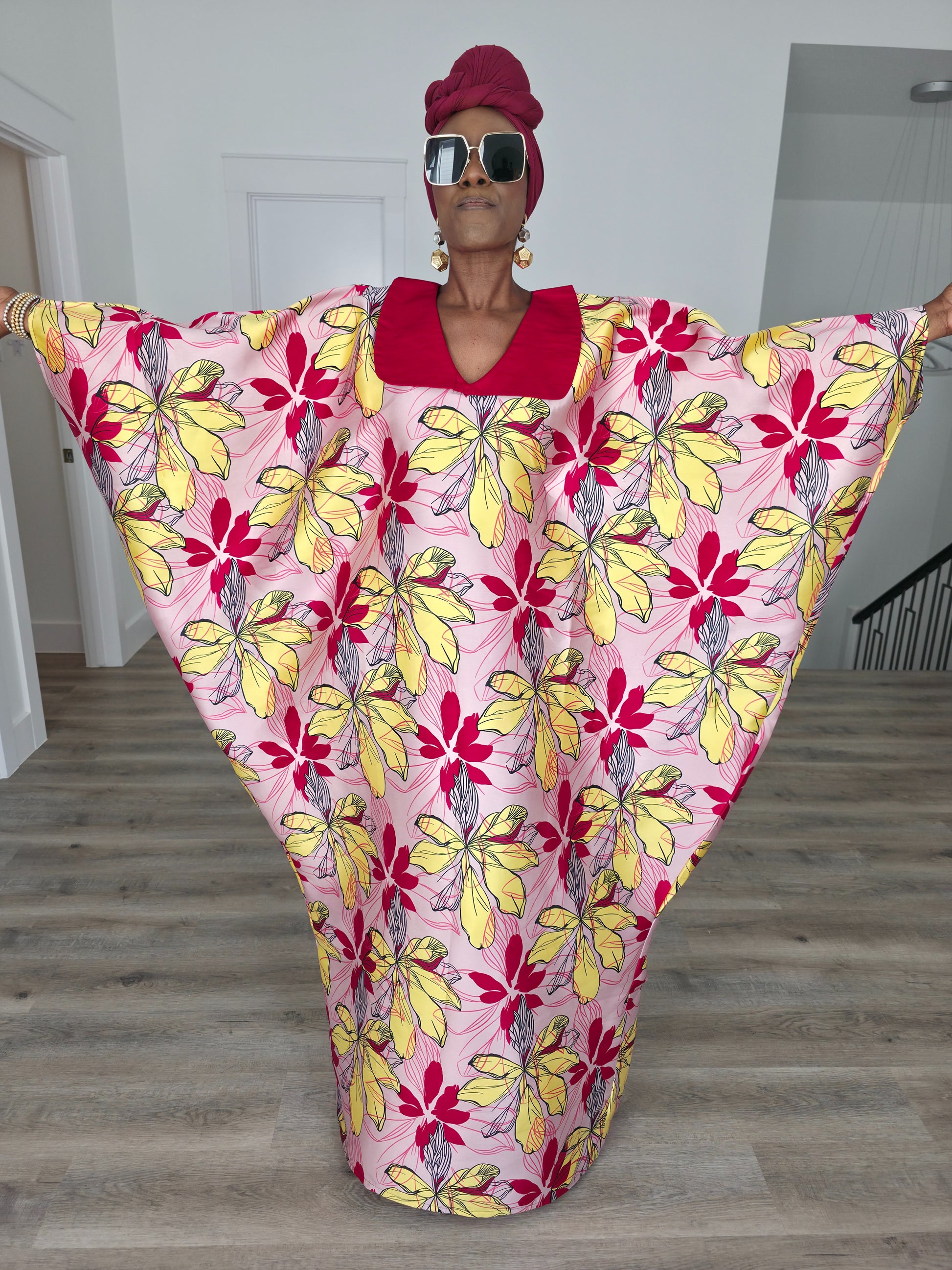 Hibiscus Sorbet Boubou Kaftan featuring a light pink fabric with large yellow and red floral prints and a structured deep red V-neck collar. Front View