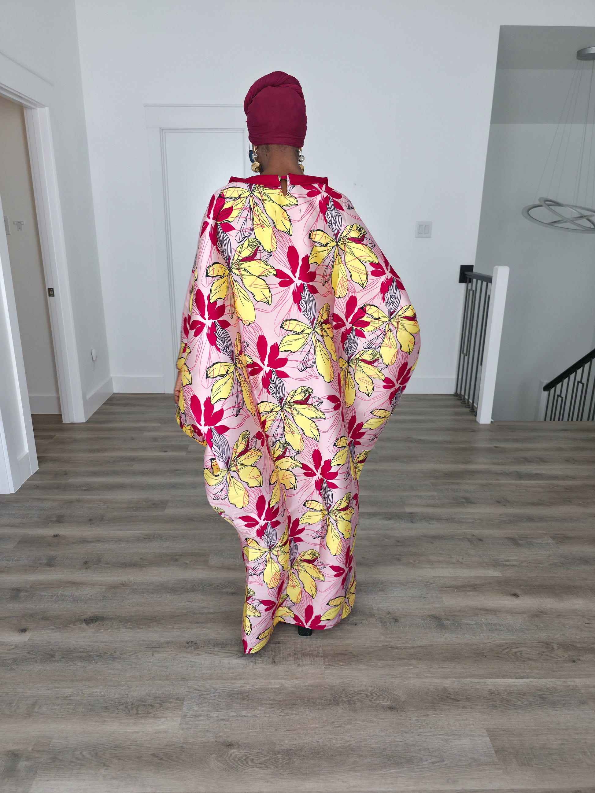Hibiscus Sorbet Boubou Kaftan featuring a light pink fabric with large yellow and red floral prints and a structured deep red V-neck collar. Back View