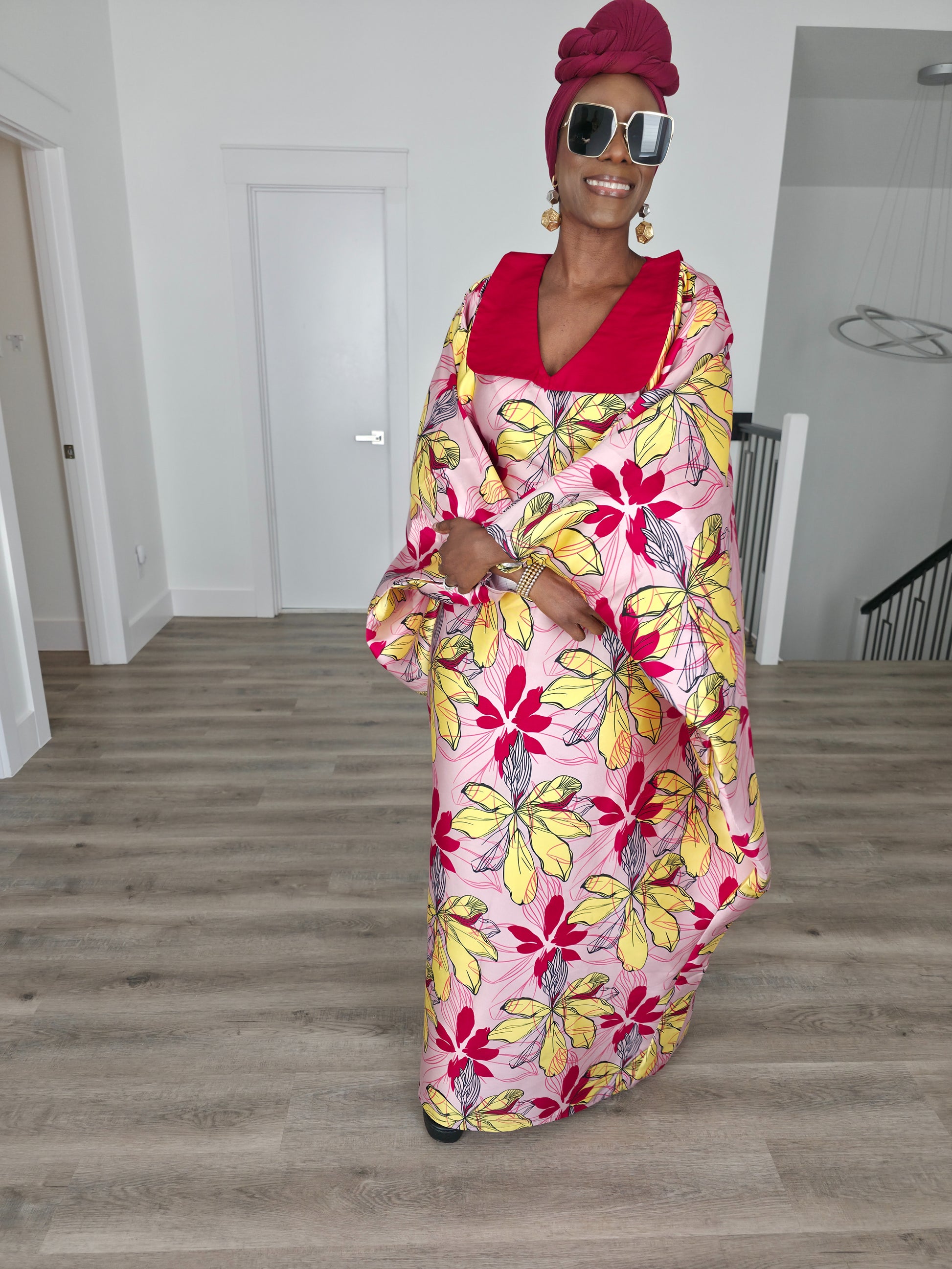 Hibiscus Sorbet Boubou Kaftan featuring a light pink fabric with large yellow and red floral prints and a structured deep red V-neck collar.