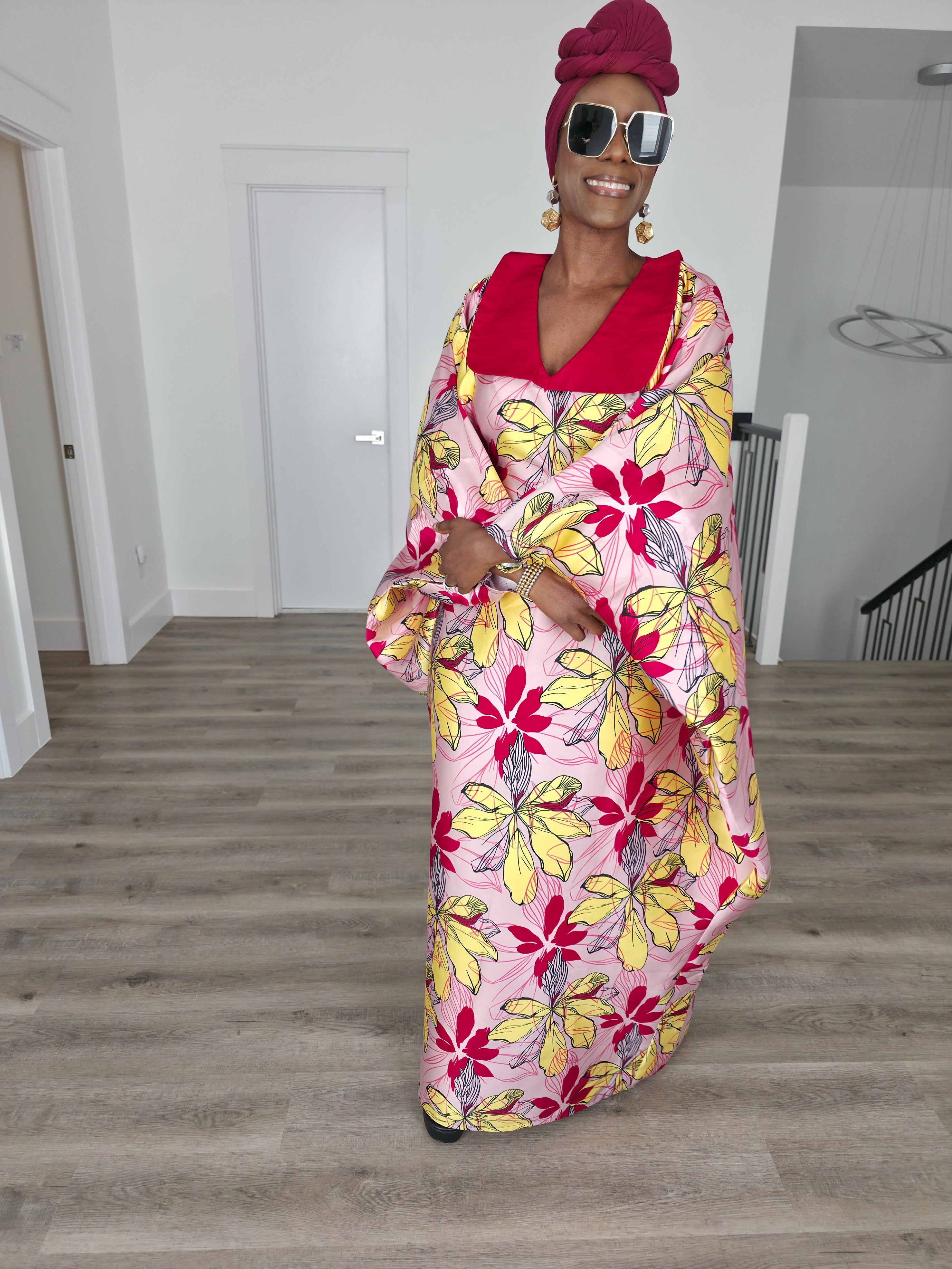 Hibiscus Sorbet Boubou Kaftan featuring a light pink fabric with large yellow and red floral prints and a structured deep red V-neck collar.