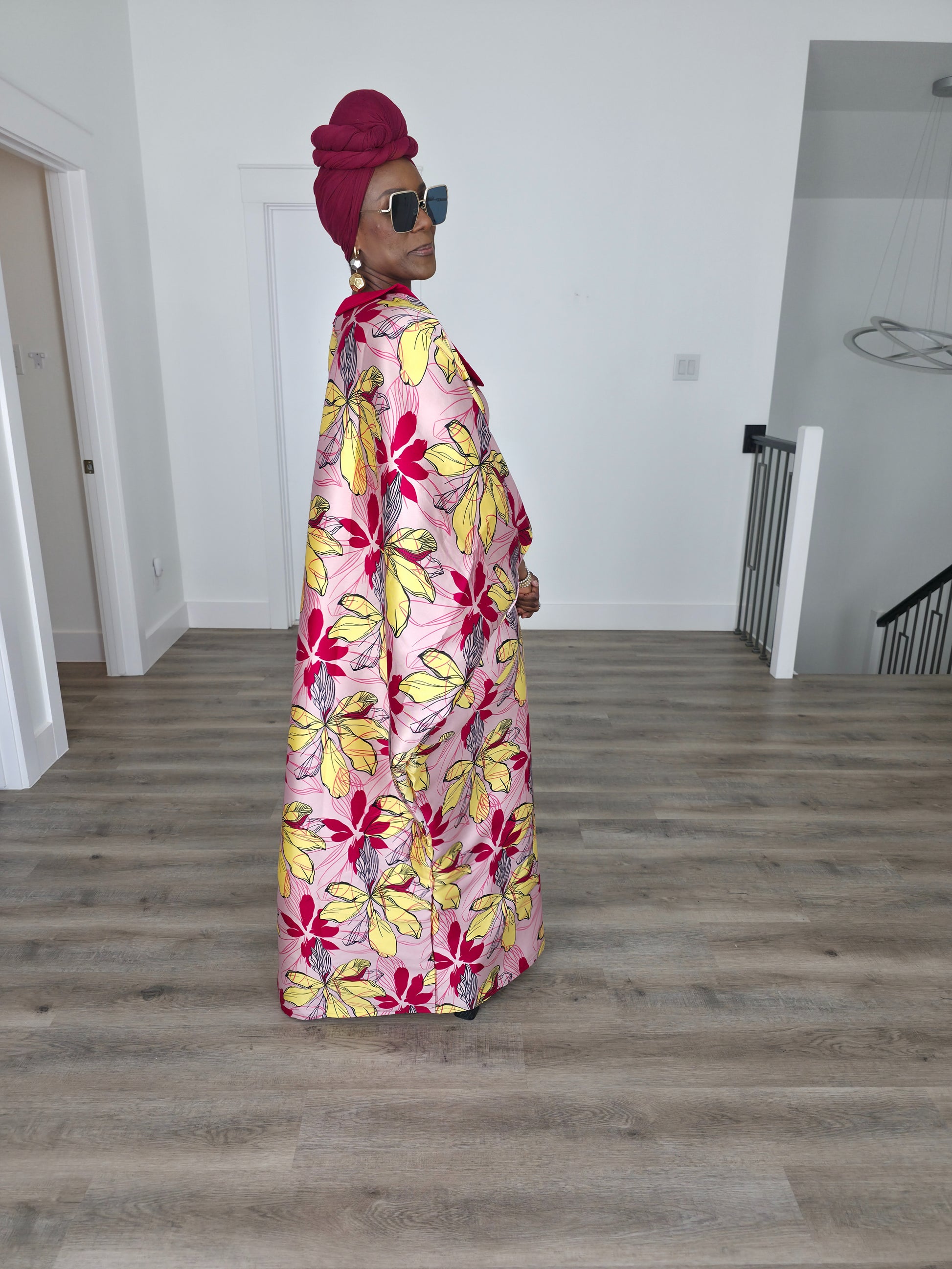 Hibiscus Sorbet Boubou Kaftan featuring a light pink fabric with large yellow and red floral prints and a structured deep red V-neck collar. Side View 
