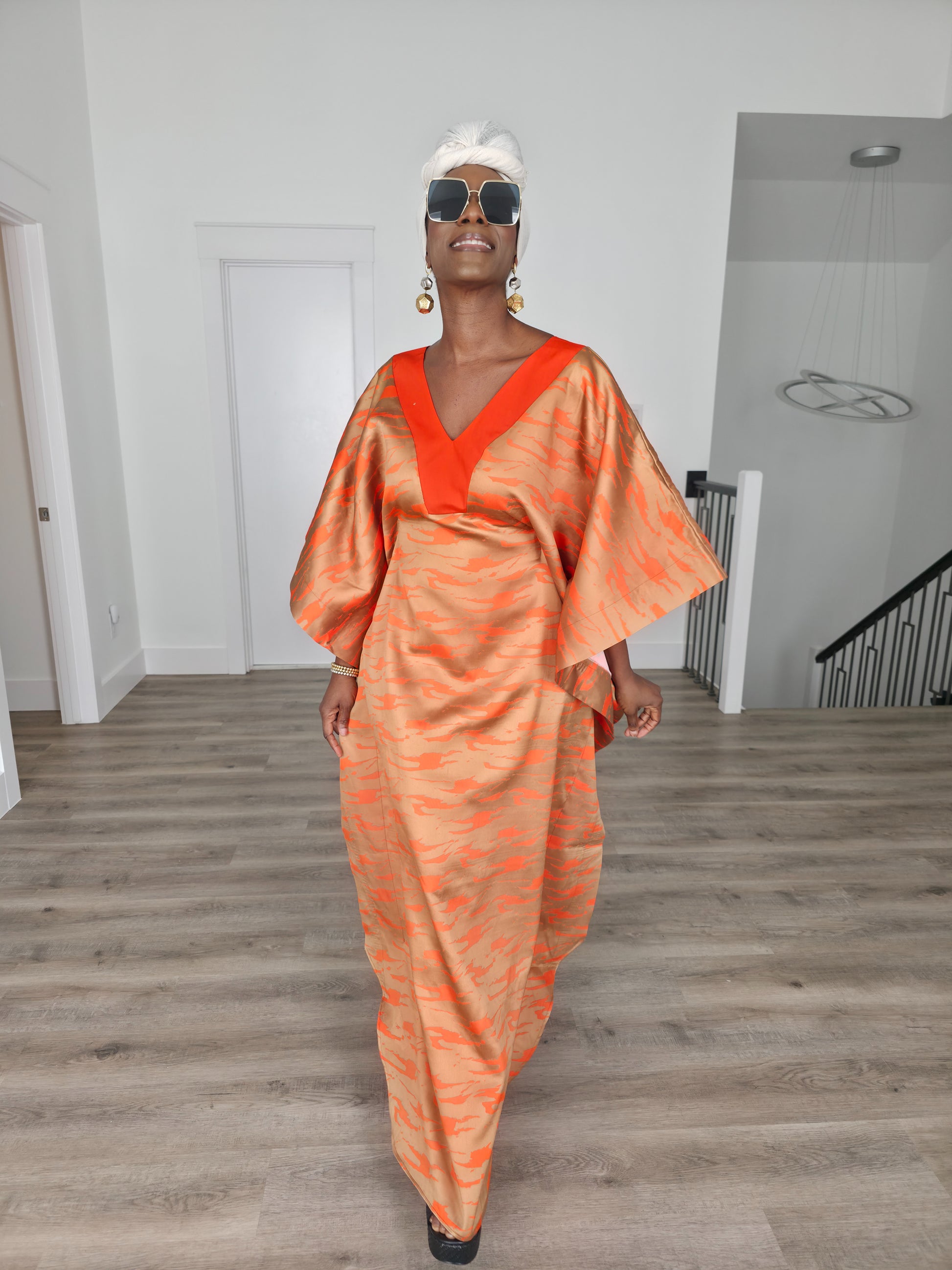 Molten Ember Boubou Kaftan in copper and orange abstract print with a solid orange V-neckline and a white headwrap. Front