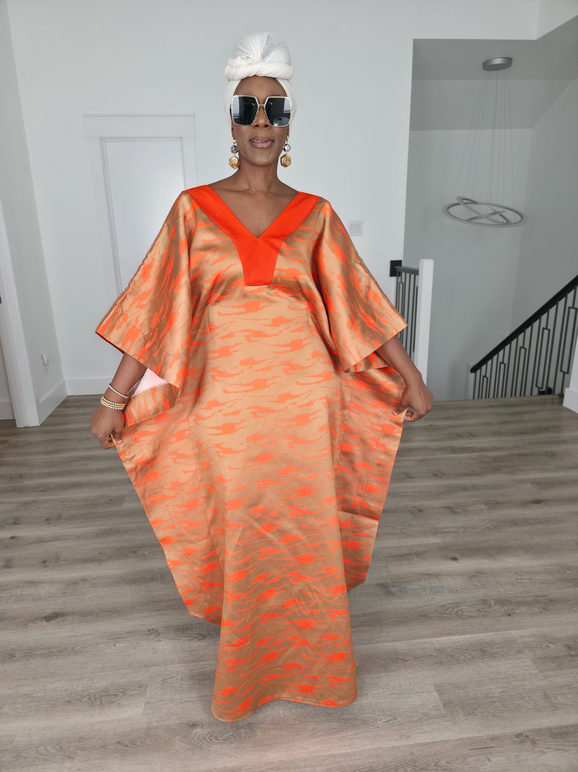 Molten Ember Boubou Kaftan in copper and orange abstract print with a solid orange V-neckline and a white headwrap. Women's Wear