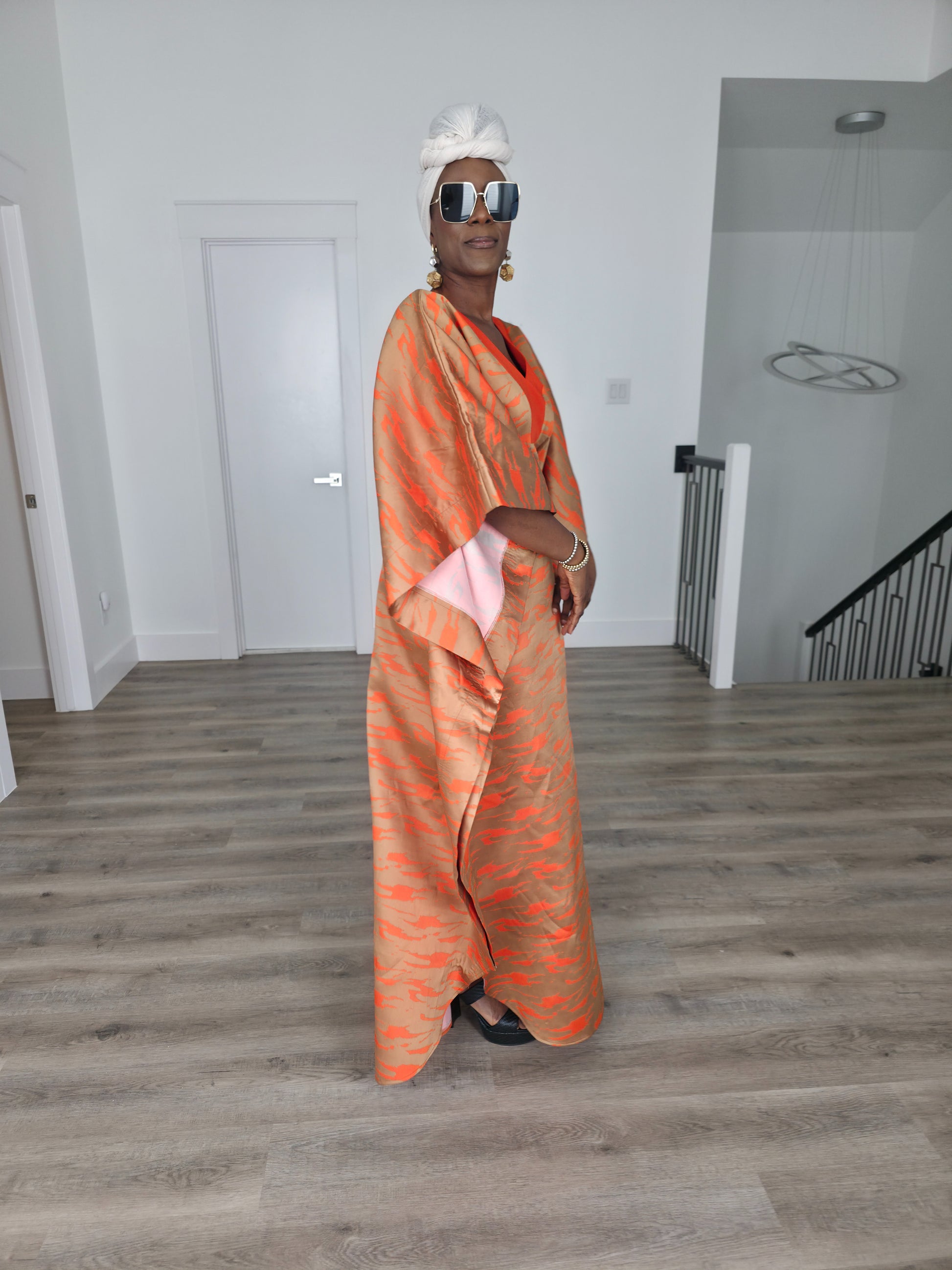 Molten Ember Boubou Kaftan in copper and orange abstract print with a solid orange V-neckline and a white headwrap. Side View