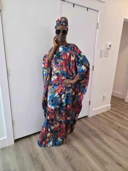 Tropical Dusk Boubou Kaftan featuring an all-over abstract floral print in blue, orange, and pink with a sophisticated off-the-shoulder neckline. 